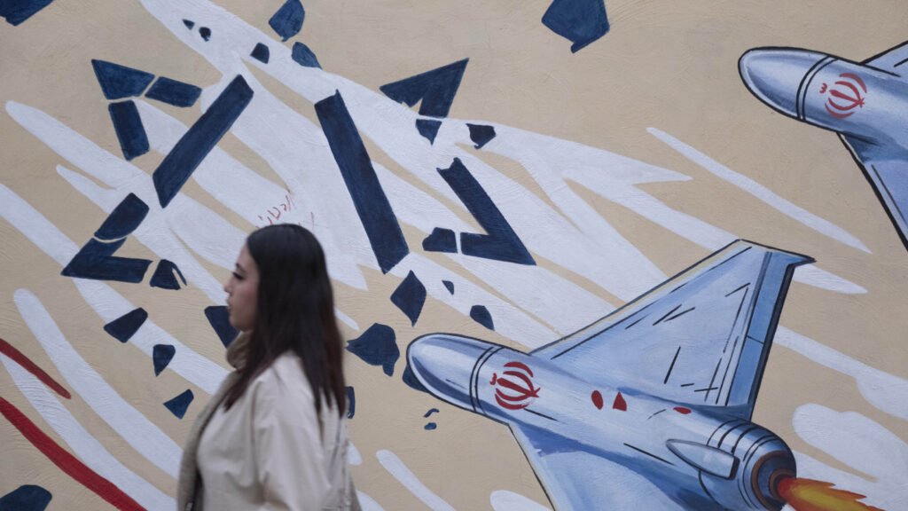 الاتفاق الأمريكي الإيراني: هزيمة استراتيجية لإسرائيل ونتنياهو A pedestrian walks past a state-sponsored political billboard on a wall in Tehran, Iran, which depicts stylized military missiles breaking a Star of David emblem, providing visual context to the geopolitical friction and discourse surrounding a strategic defeat for Israel.