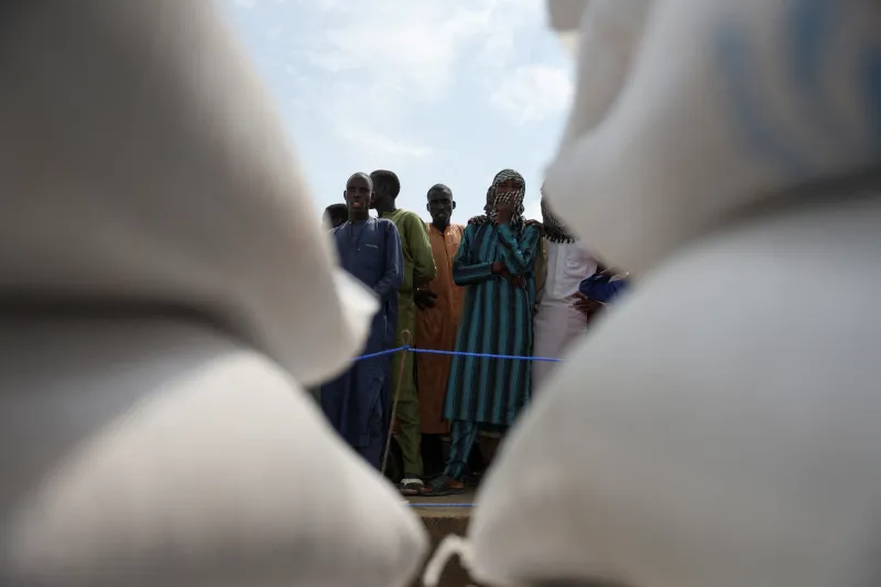 The End of Foreign Aid Is Not the End of Development A low-angle view framed between large white supply sacks showing a crowd of local people waiting at a World Food Program distribution centre in Dikwa, Nigeria, highlighting the systemic challenges surrounding Foreign Aid.