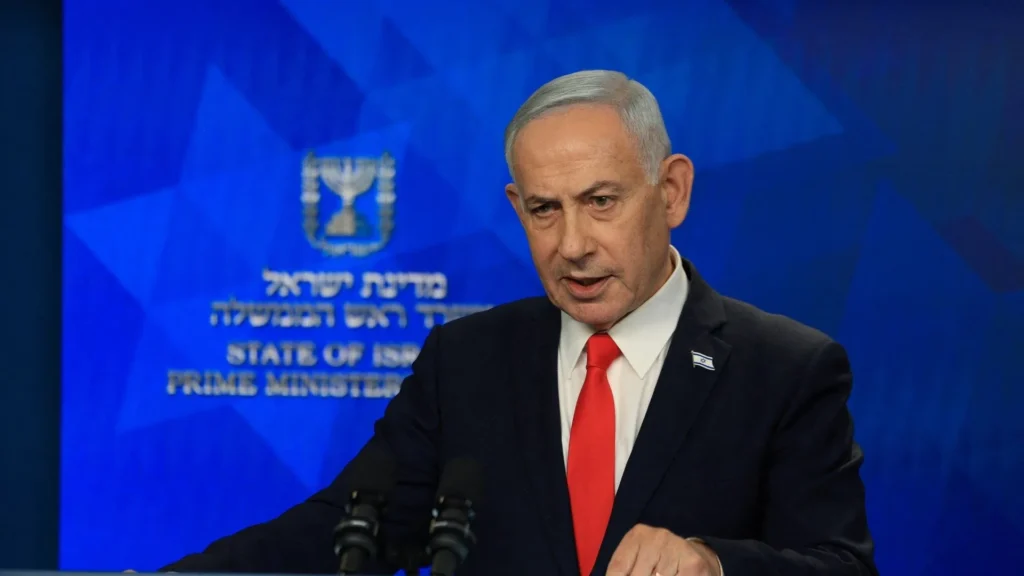 Israeli Prime Minister Benjamin Netanyahu in a dark suit and red tie speaking at a podium against a blue backdrop featuring the State of Israel Prime Minister emblem, capturing the political tension surrounding the Lebanon Dilemma.