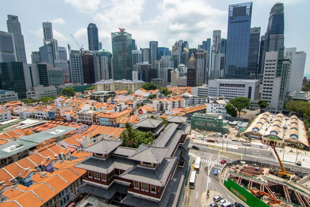 An elevated view contrasts the ornate, tiered traditional roofs of a historic temple and low-rise orange-tiled neighborhood with a towering backdrop of ultra-modern corporate skyscrapers, visually symbolizing how structural economic dynamics sustain inequality.