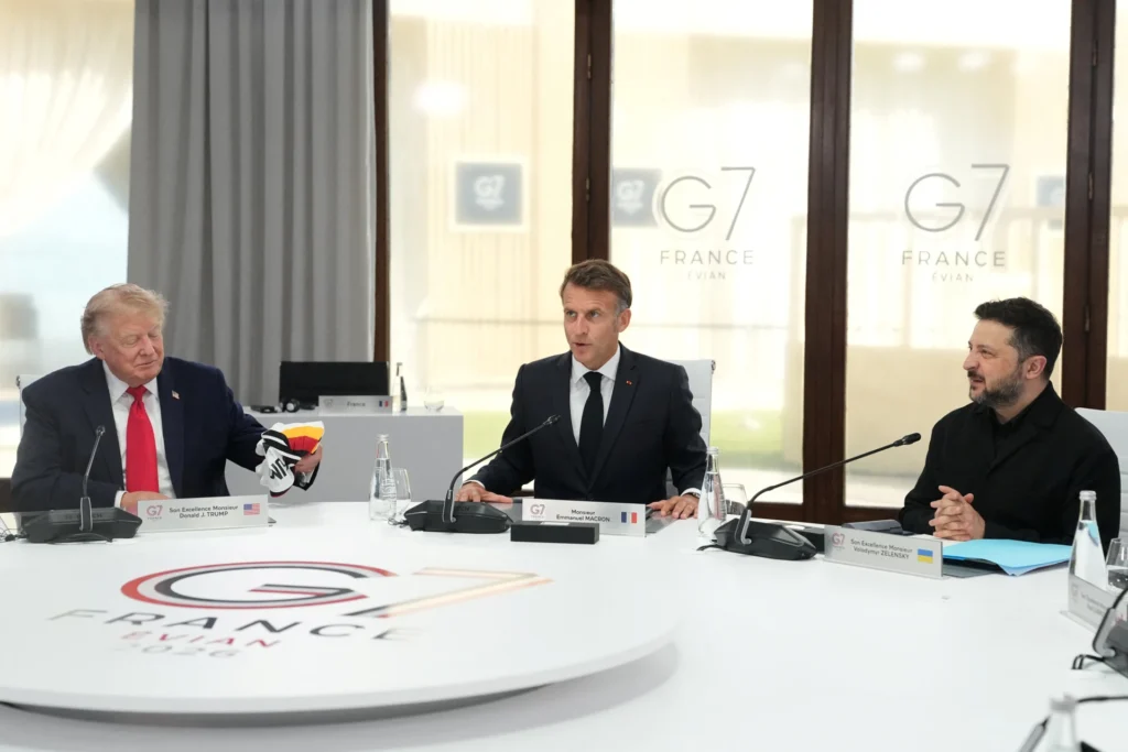 US President Donald Trump, French President Emmanuel Macron, and Ukrainian President Volodymyr Zelenskyy seated around a round summit table at the G7 France Evian 2026 meeting, highlighting complex multilateral discussions that test The G7's Alignment.