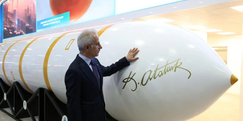 A Turkish official in a suit standing next to and touching the nose cone of the Yildirimhan intercontinental ballistic missile featuring the signature of Mustafa Kemal Atatürk on display, highlighting the regional defense developments surrounding Turkey's new missile.
