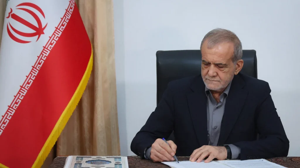 Iranian President Masoud Pezeshkian sitting at a desk next to the Iranian flag while signing a document, an official act concluding the events following the war on Iran.
