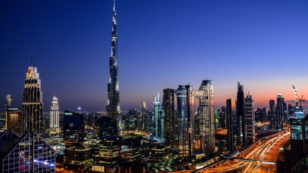 The illuminated skyline of Dubai at dusk, featuring the Burj Khalifa and modern skyscrapers next to a busy highway, visually contextualizes the regional stability at stake for Gulf Security.