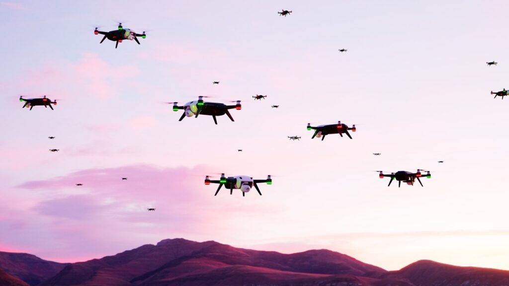 A digital rendering of a large swarm of quadcopter drones flying in midair over a rugged mountain ridge against a pink sunset sky, conceptually illustrating allegations regarding the deployment of tactical Jellyfish Drone Swarms.