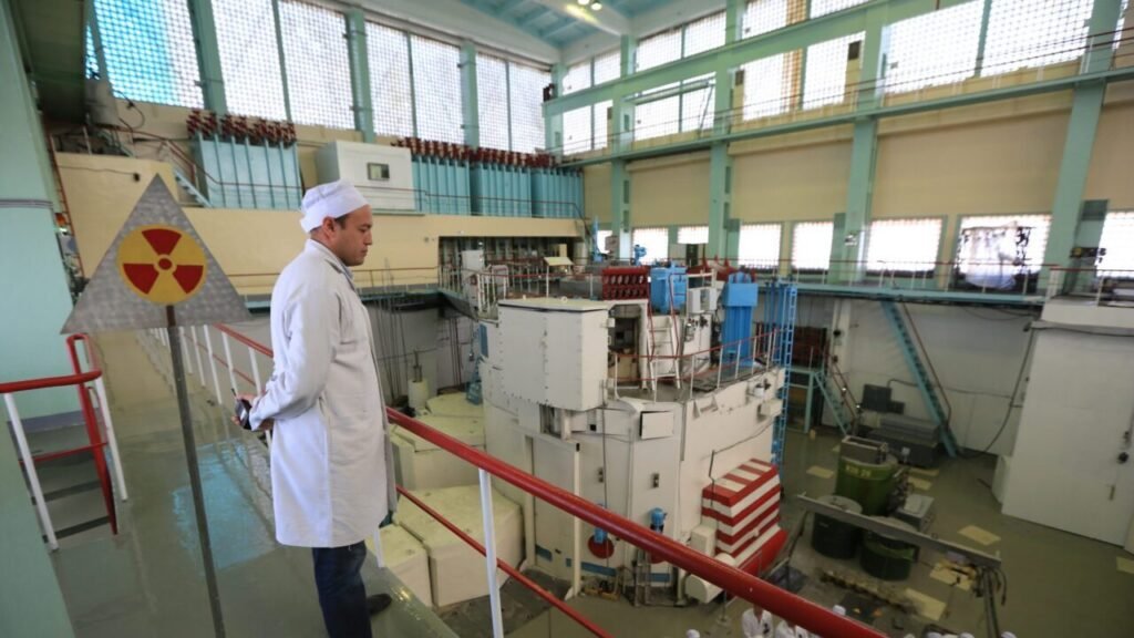 چگونه قزاقستان میتواند به نهایی شدن توافق هستهای ایران کمک کند A technician in a white lab coat and cap looks down from a railed balcony at a large nuclear research reactor facility, illustrating the strategic atomic infrastructure central to discussions on how Kazakhstan Help Iran Nuclear Deal.
