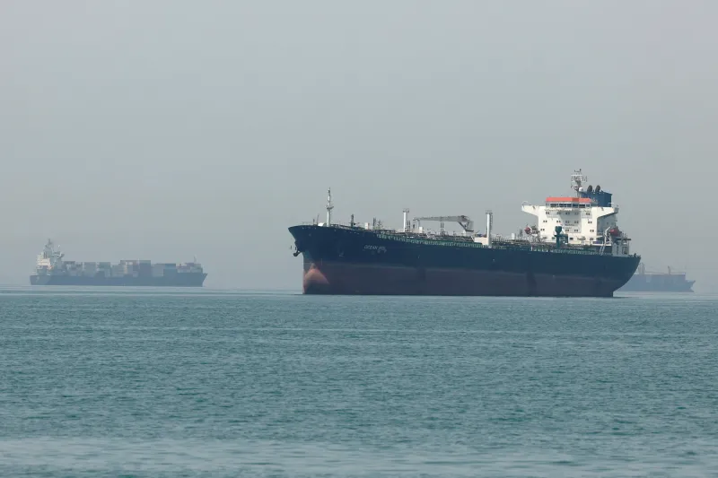 كيف فقدت أمريكا السيطرة على المشاعات A large commercial oil tanker and several distant cargo ships traverse the calm waters of the Strait of Hormuz under a hazy sky, highlighting the critical maritime chokepoints connected to the debate over How America Lost command of the commons.