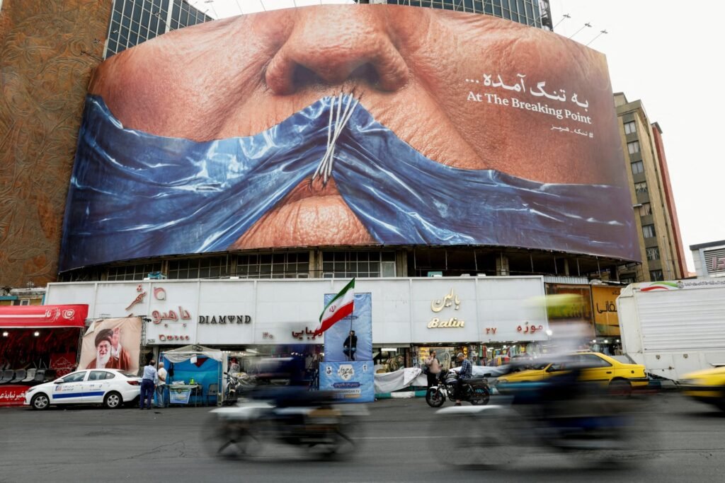 A large public billboard in Tehran displays an anti-U.S. graphic depicting U.S. President Donald Trump’s face with blue fabric stitched over the mouth to symbolize the Strait of Hormuz, providing a prominent urban backdrop to evaluate whether a U.S.-Iran Deal Within Reach.