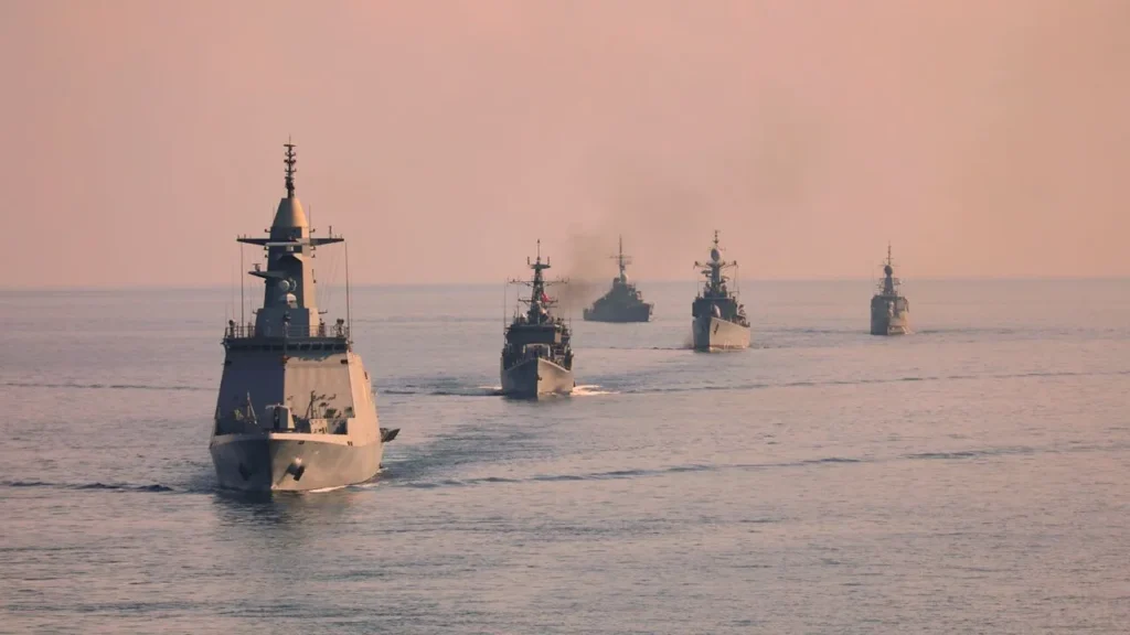 How to Fight the U.S Navy on the Cheap A flotilla of naval ships in formation on open water, visually representing the maritime presence and strategic challenges faced by the U.S Navy.