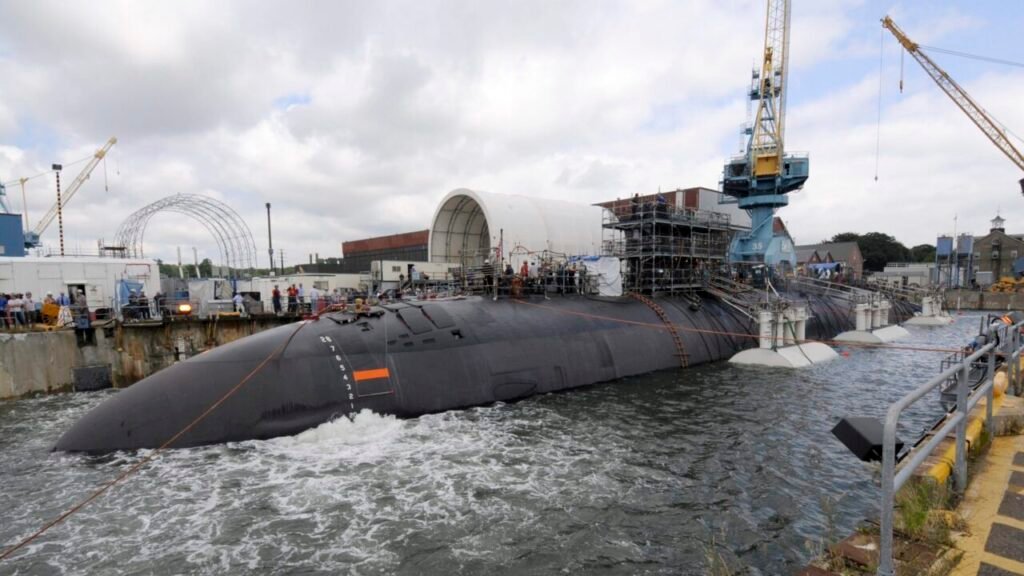كيف تؤثر التعريفات الجمركية على تسريع بناء السفن في البحرية الأمريكية A wide-angle shot of the Los Angeles-class submarine USS San Juan floating in a drydock at Portsmouth Naval Shipyard, surrounded by workers, heavy construction scaffolding, and a large blue crane marked with the number 35, illustrating the industrial challenges linked to the US Navy's Shipbuilding Surge.