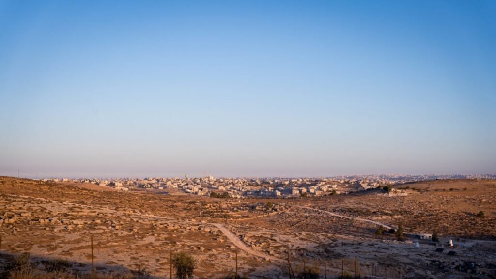 Panoramic sunset view over the rocky landscape and residential settlements across the West Bank, reflecting territorial dynamics related to the War on Palestine.
