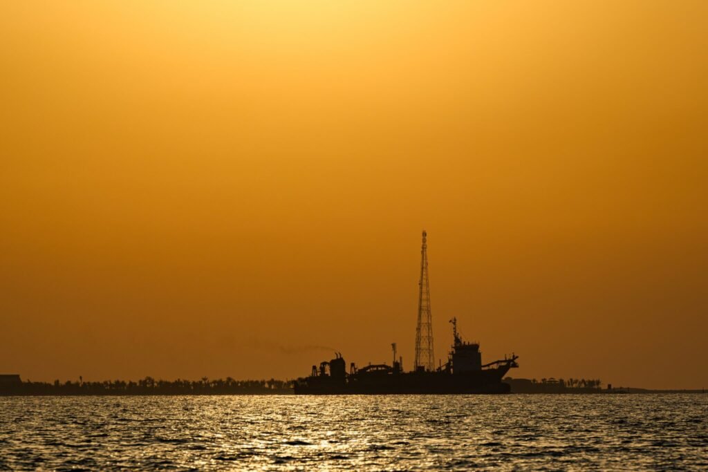 Strait of Hormuz conflict: 3 future scenarios A silhouette of a ship with a tall mast on the water during a golden sunset, symbolizing the critical maritime infrastructure at the heart of the Strait of Hormuz conflict.
