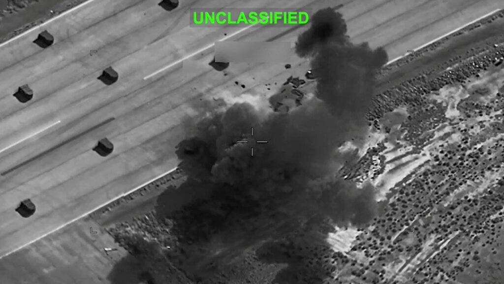 The U.S.-Iran Memorandum of Understanding on Life Support An aerial, black-and-white surveillance screen grab showing smoke rising from an explosion at an undisclosed location, visually underscoring the instability surrounding the Iran Memorandum.