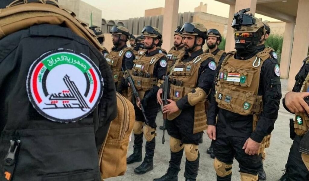 Iraqi Popular Mobilization Forces fighters in tactical gear standing in formation with a visible Hashd al-Shaabi patch, reflecting security dynamics surrounding the Iraq Militia Threat.