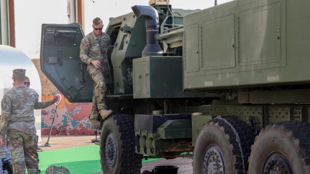 A U.S. soldier climbing down from a heavy military vehicle cab during a defense exhibition, illustrating security posture and geopolitical dynamics related to the Jordan Gambit.
