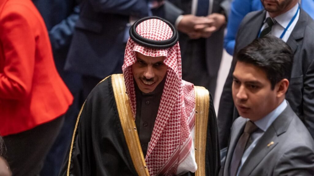 Why Is Saudi Arabia Appeasing Iran? Saudi Foreign Minister Faisal bin Farhan Al Saud wearing a traditional red and white keffiyeh and a black bisht with gold trim walks through a crowded diplomatic venue, highlighting the complex regional shifts related to Saudi Arabia Appeasing Iran.