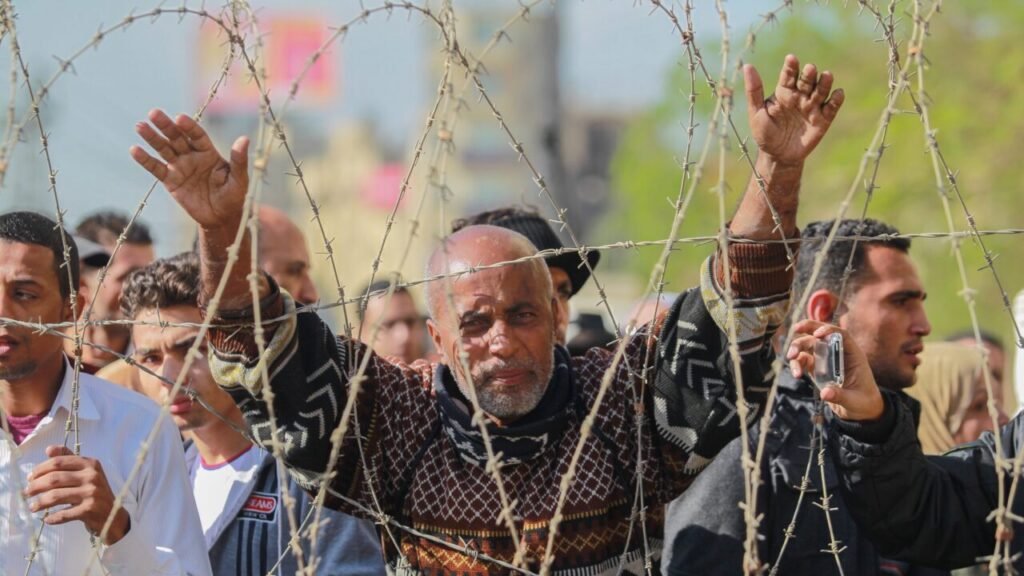 The End of Political Islam? Not Quite An elderly man with a concerned expression raising his hands behind a barrier of coiled barbed wire during an Egyptian protest against the military coup, capturing the struggle and grievances associated with the decline of Political Islam.