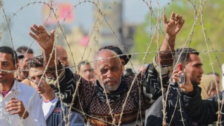 An elderly man with a concerned expression raising his hands behind a barrier of coiled barbed wire during an Egyptian protest against the military coup, capturing the struggle and grievances associated with the decline of Political Islam.