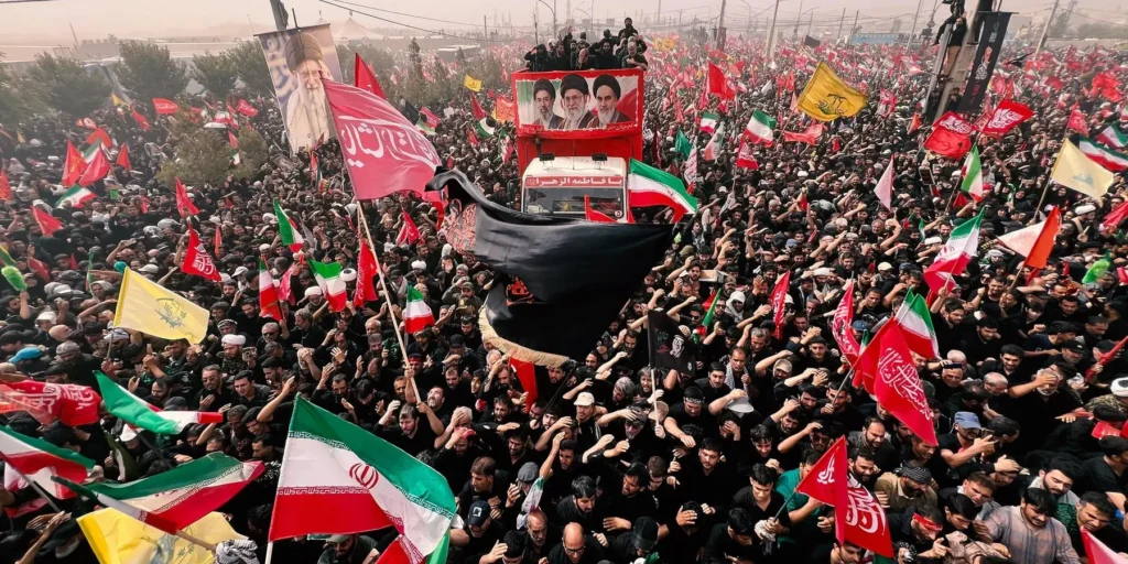 An overhead view of a massive crowd of people wearing black, carrying Iranian, yellow, and red flags during a funeral procession surrounding a red truck with a portrait banner, capturing the atmosphere of public mourning for Ayatollah Khamenei.