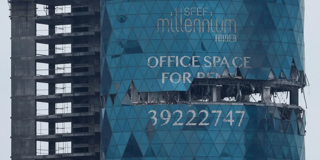 Iran Gulf Attacks: How Tehran Shoots Itself in the Foot Visible structural damage on the blue glass facade of the Millennium Tower skyscraper with blown-out office floors, highlighting urban infrastructure impact caused by Iran Gulf Attacks.