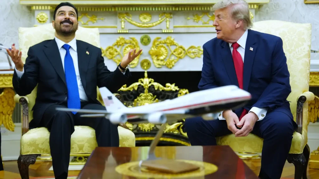 A medium shot of U.S. President Donald Trump and Iraqi Prime Minister Ali al-Zaidi engaged in a formal discussion in the White House, with a model airplane in the foreground, highlighting the diplomatic context of ongoing Iraq sanctions.