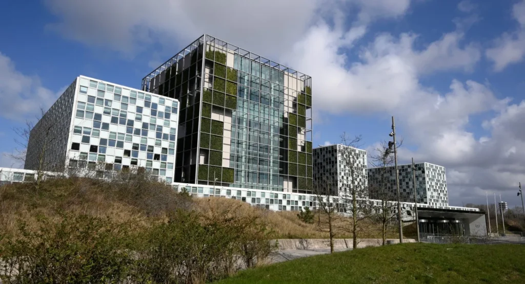 A wide exterior view of the International Criminal Court (ICC) building in The Hague, featuring its modern glass and grid architecture, representing the institution currently facing a push to Dismantle the ICC.