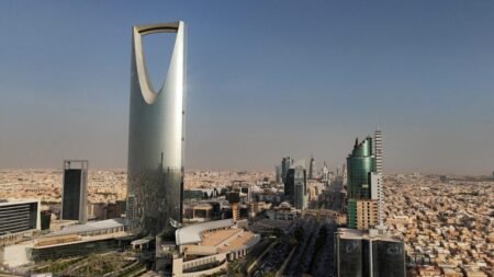 A high-angle drone view capturing the modern cityscape of Riyadh, dominated by the iconic Kingdom Centre skyscraper alongside other high-rise buildings and surrounding urban development under a clear sky, highlighting areas built through Economic Resiliency.