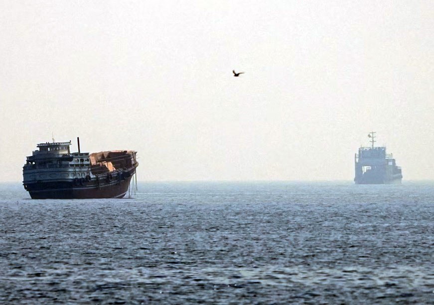 أزمة مضيق هرمز تعيد إشعال المخاوف العالمية من الطاقة A wooden dhow and a commercial vessel navigating calm, hazy open waters, illustrating maritime trade routes associated with the Strait of Hormuz crisis.