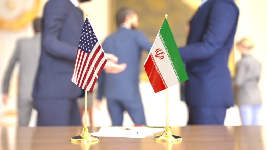 The First Post-Heroic War: The “Boots on the Ground” Syndrome Small table flags of the United States and Iran sitting side by side on a wooden desk with blurred diplomats meeting in the background, illustrating geopolitical negotiations and Post-Heroic War.