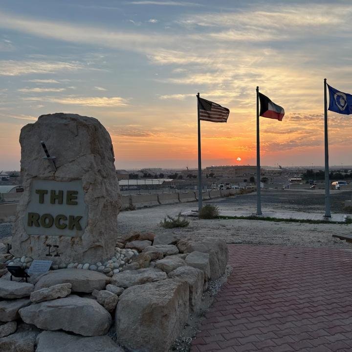 US-Kuwait Partnership Faces a Critical Postwar Test The American and Kuwaiti national flags flying side-by-side at sunset near "The Rock II" stone monument at Ali Al Salem Air Base, representing strategic cooperation within the US-Kuwait Partnership.