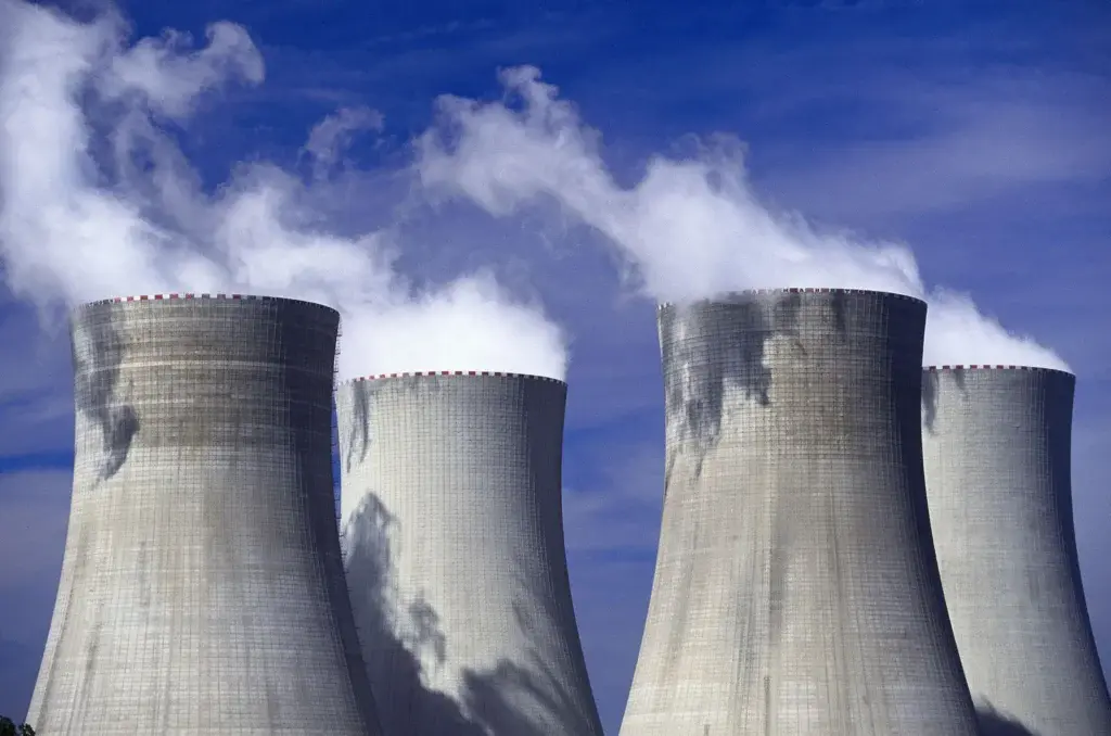 Gulf Nuclear Competition Begins With the US Saudi Deal Four large concrete nuclear power plant cooling towers emitting steam into a blue sky, reflecting energy infrastructure developments in the Gulf Nuclear Competition.