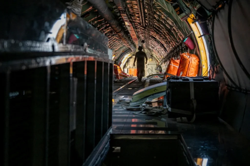 17 Dead: US Bases Near Iran Force a Strategic Rethink A view inside the cargo hold of a U.S. military aircraft as a crew member walks down the interior bay, illustrating troop movements and logistics regarding US Bases Near Iran.