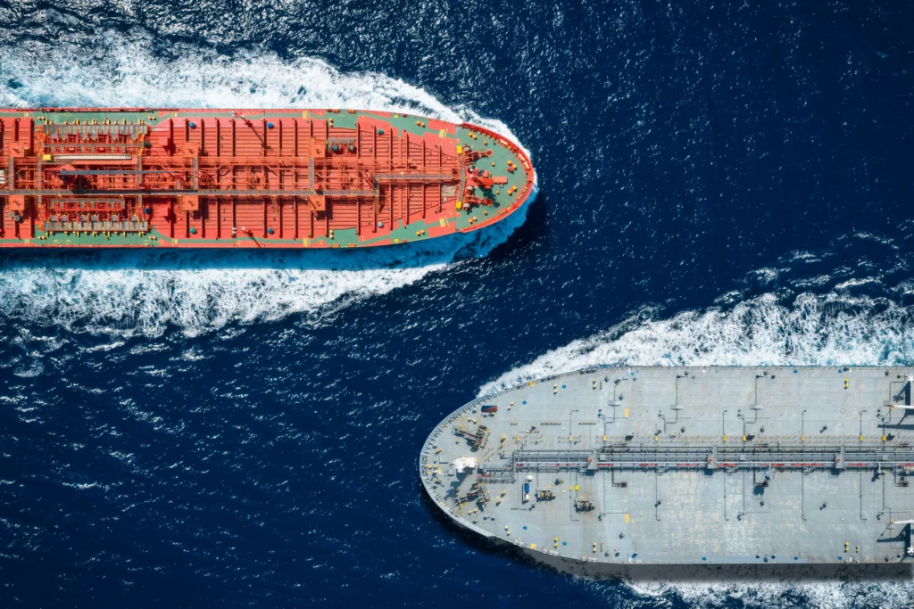 With US sanctions temporarily lifted, is Iranian crude back on the menu? An overhead aerial view of two large oil tankers navigating close to each other through deep blue ocean waters, leaving distinct white wakes behind them, representing the global maritime trade dynamics surrounding Iranian crude.