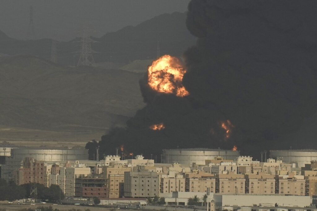 Heavy black smoke and a massive fireball rising from oil storage facilities following an attack near residential buildings and mountains, highlighting threats to the Saudi Pipeline.