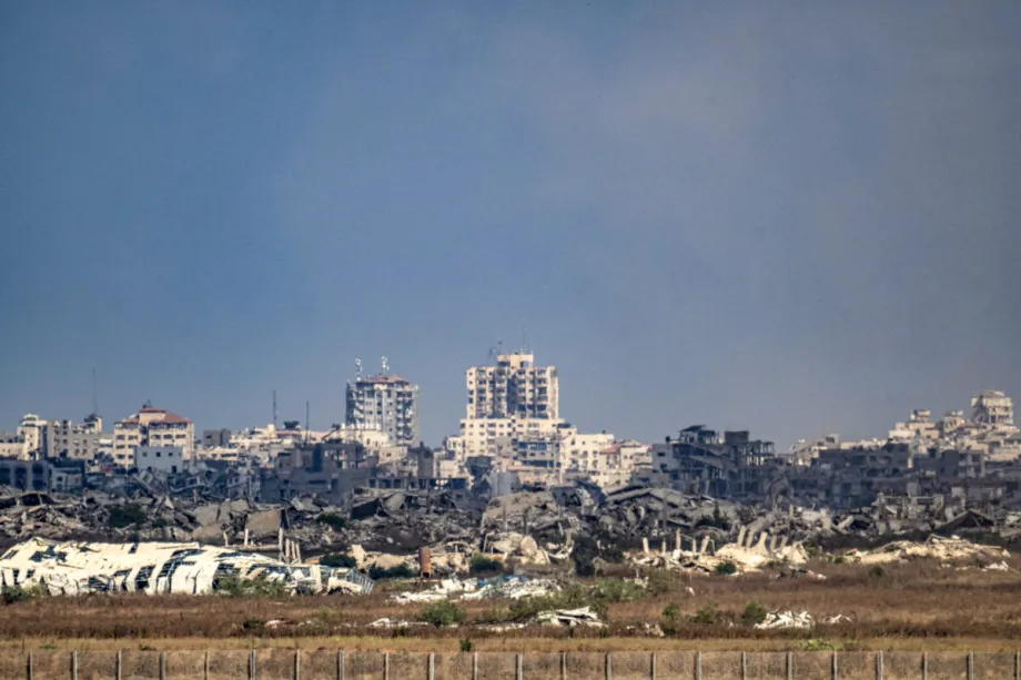 Hamas is leaving government, not the resistance A wide, distant view of the heavily damaged skyline of Gaza, showing fractured high-rise buildings standing amidst fields of rubble under a clear blue sky, illustrating the impact of conflict linked to the concept of resistance.