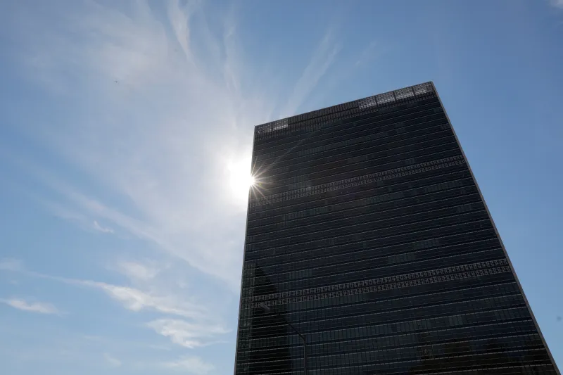 How to Save the UN From Irrelevance A low-angle view looking up at the glass facade of the United Nations Secretariat Building with the sun glinting off its edge against a blue sky with light clouds, providing visual context for discussions on how to Save the UN.