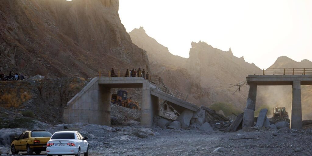 الأفكار المتفائلة وراء الحرب مع إيران People standing near a damaged concrete bridge in a mountainous region of Hormozgan province, illustrating infrastructure destruction during the war with Iran.