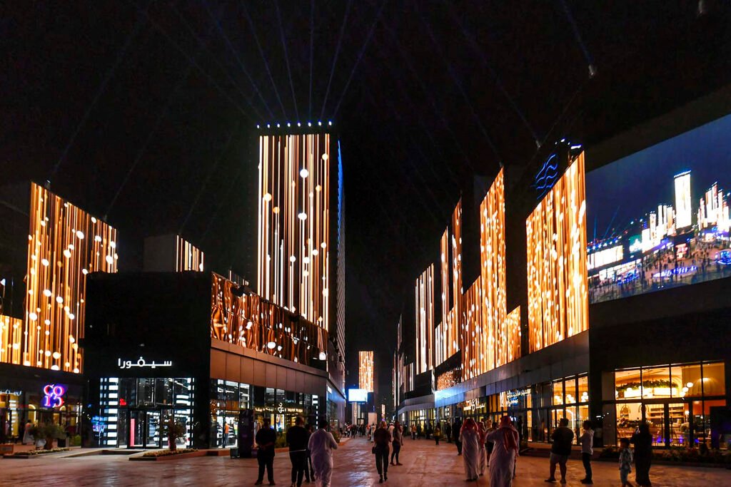 Have Saudi Labor Market Reforms Run Their Course? Pedestrians walking through a brightly illuminated modern commercial complex at night in Saudi Arabia, reflecting economic developments within the Saudi Labor Market.