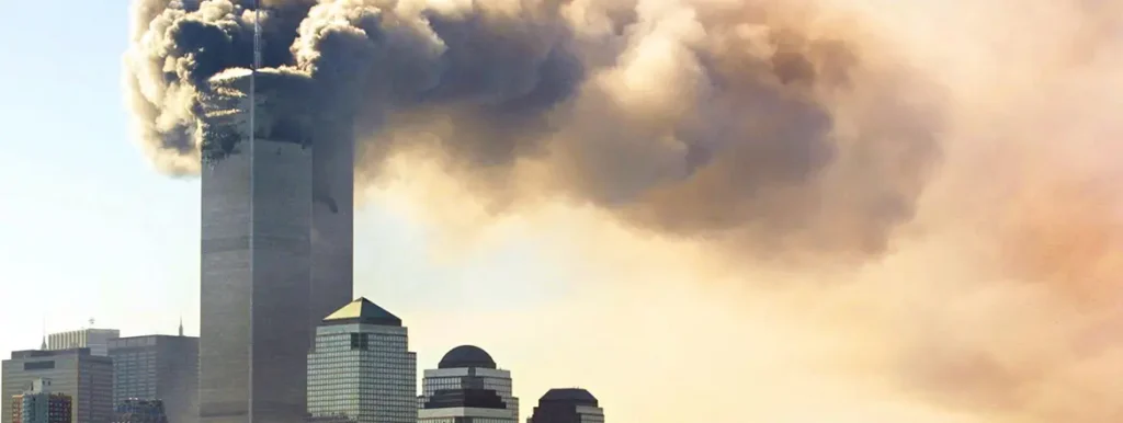 A wide view of the World Trade Center towers in New York City with thick, heavy smoke billowing out from the upper floors across the sky, captured above the lower Manhattan skyline during an event that historical analyses compare to a potential future Global Shock.