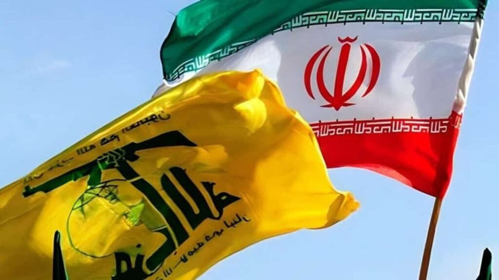 The yellow flag of Hezbollah with its green emblem waves prominently alongside the national flag of Iran against a clear blue sky, capturing the geopolitical alliance relevant to the discussion around the US deal.