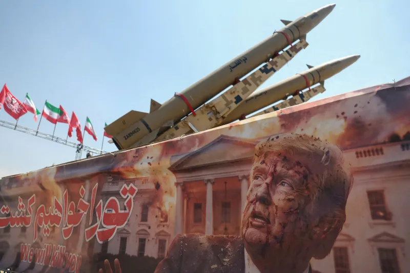 Iran War Ambiguity Fuels Escalation and Diplomatic Failure Two Iranian ballistic missiles mounted on a launcher in front of an anti-American banner depicting Donald Trump at Azadi Square in Tehran, highlighting geopolitical tensions linked to Iran War Ambiguity.