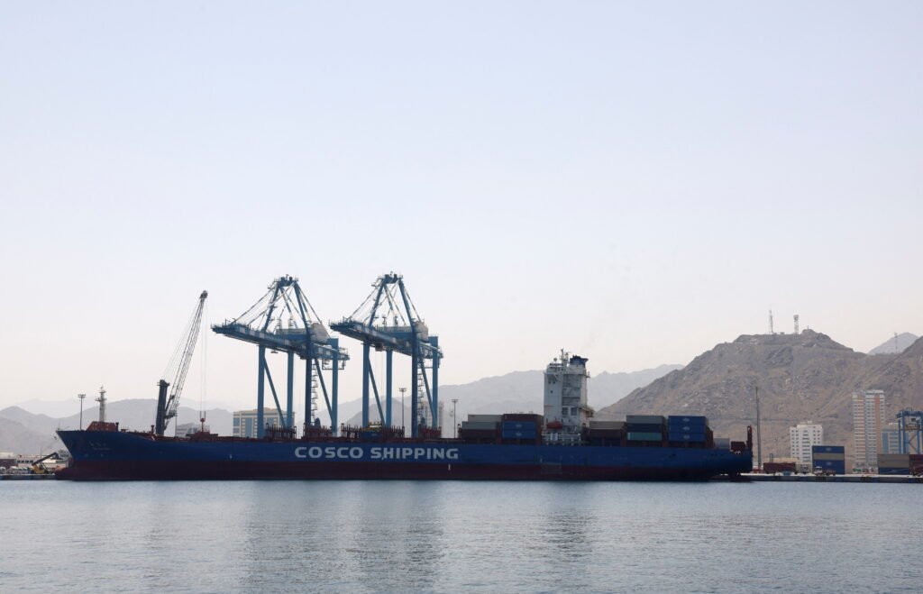 پس از بحران هرمز، بازگشتی به وضعیت موجود نیست A large COSCO SHIPPING cargo vessel docked at a commercial port terminal with high gantry cranes loading shipping containers against a mountainous coastal background, highlighting maritime trade routes affected by the Hormuz crisis.