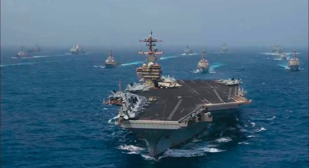تجاوز مجدد ایران باید ایالات متحده را به احیای کمپین فشار حداکثری ترغیب کند A wide-angle aerial shot of a United States aircraft carrier leading a naval strike group through open waters, demonstrating the military capabilities intended to support a renewed Maximum Pressure Campaign.