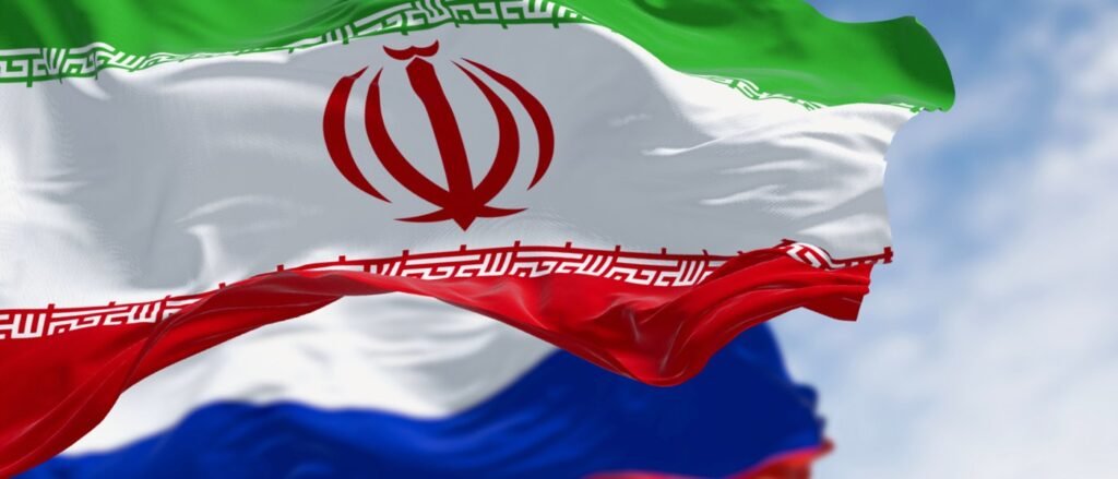 Understanding Russia-Iran Collaboration in Cyberspace A close-up view of the Iranian flag waving in the foreground, with the Russian flag partially visible and blurred behind it, symbolizing the strategic Russia-Iran partnership.