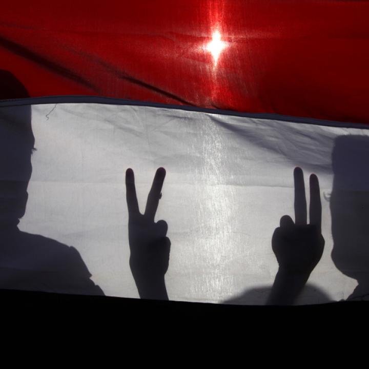 Yemen’s Truce at Risk A silhouetted image showing shadows of hands making peace signs cast against a flag, symbolizing the fragile state of Yemen's Truce.