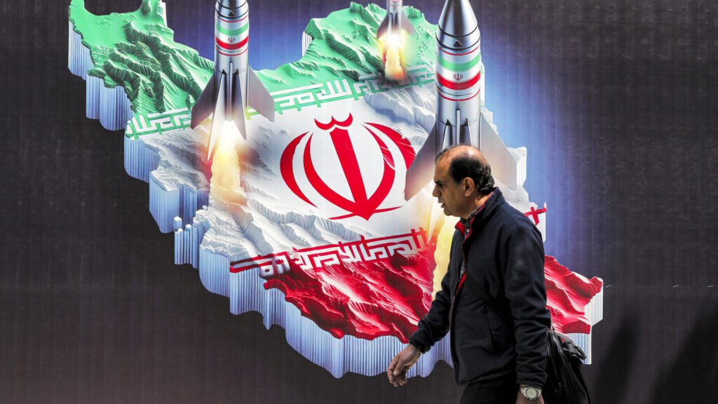 A man walks past a large street mural depicting a three-dimensional map of Iran painted with the national flag, from which several military missiles are launched with visible fire and smoke, highlighting defense capabilities related to Iran's missile programme.