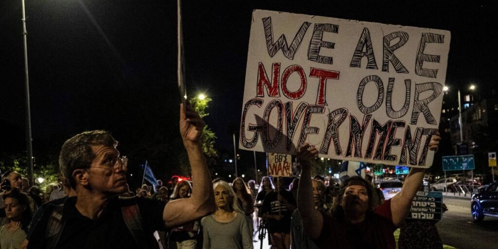 Demonstrators holding placards with protest slogans during a nighttime rally in West Jerusalem, reflecting public sentiment leading up to Israel's general election.