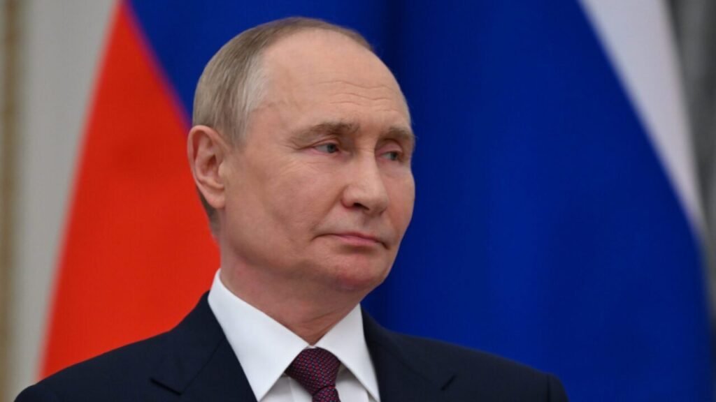 Russian Mediation Breaks US-Iran Nuclear Deadlock A close-up portrait of Russian President Vladimir Putin in a dark suit and patterned red tie, looking off-camera with a serious, contemplative expression against the blurred red and blue backdrop of the Russian flag, visually representing the pivotal diplomatic role of Russian Mediation in successfully breaking the prolonged US-Iran nuclear deadlock.