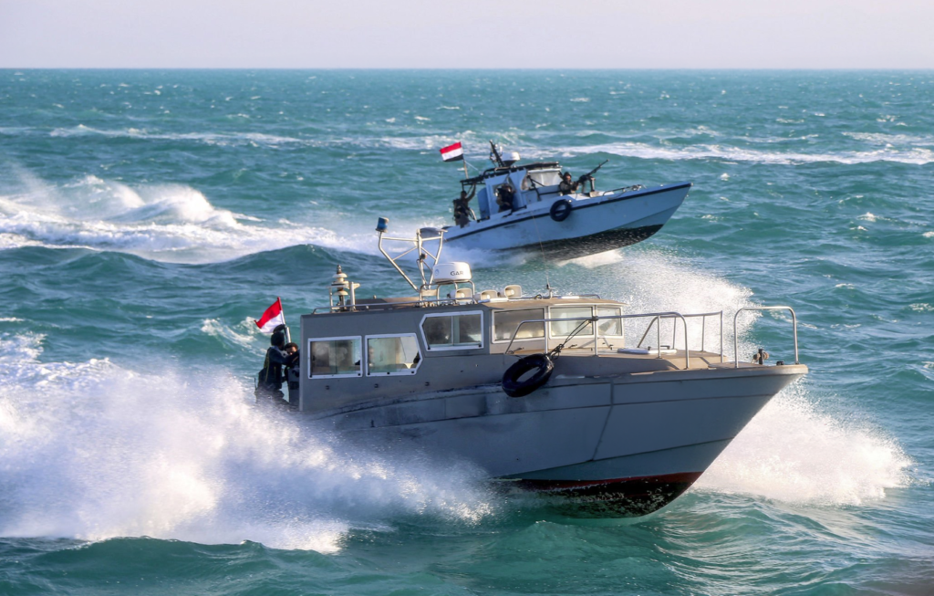 Yemen Maritime Forces Counter Houthi Smuggling A dynamic maritime photograph of Yemeni coastguard members riding in a grey speedboat and a larger patrol boat, flying the Yemeni flag while speeding through choppy Red Sea waters off Mokha, illustrating the active interdiction patrols of Yemen Maritime Forces to counter Houthi smuggling near the strategic Bab al-Mandab Strait.