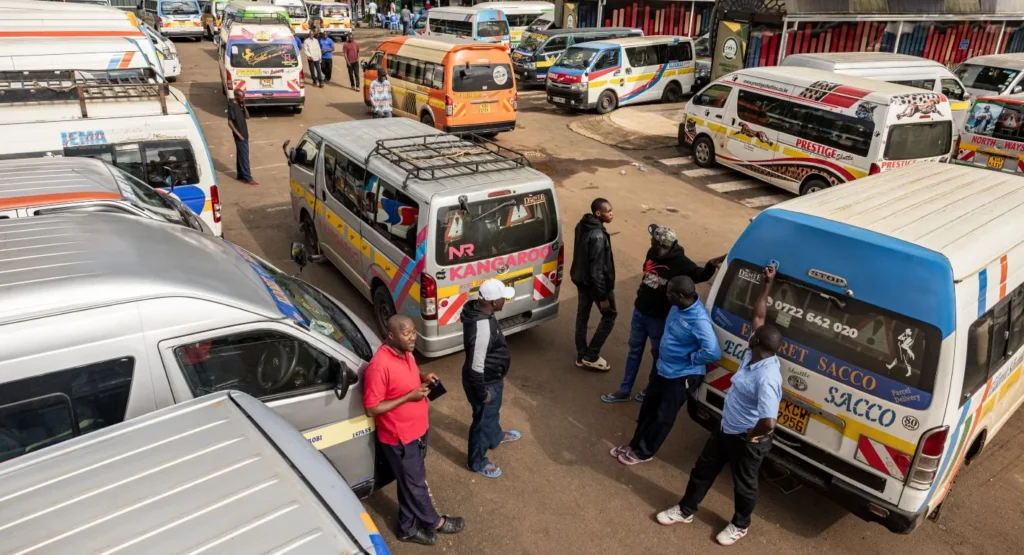 A crowded transport depot in Nairobi packed with colorful matatu minibuses, where transit workers stand idle and wait beside their vehicles, representing the nationwide strike over fuel price increases that underscores the severe economic strain of the Kenya Fuel Crisis threatening President Ruto's reelection bid.